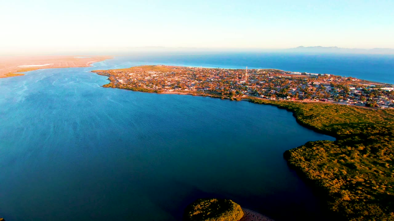 High aerial view of coastal water, green shoreline, and town buildings.
