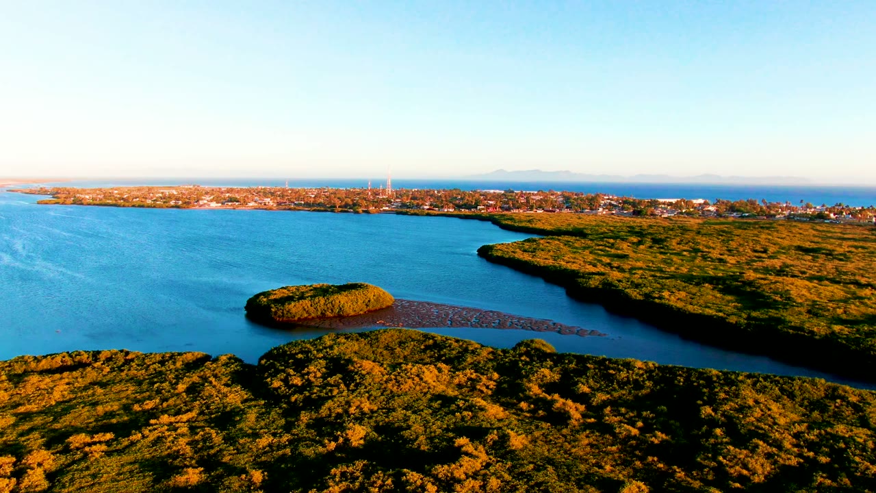 Midway through the opening row, the aerial view shows the small vegetated island-like form more clearly against the bay, with San Carlos town buildings on the far shore and no visible people.