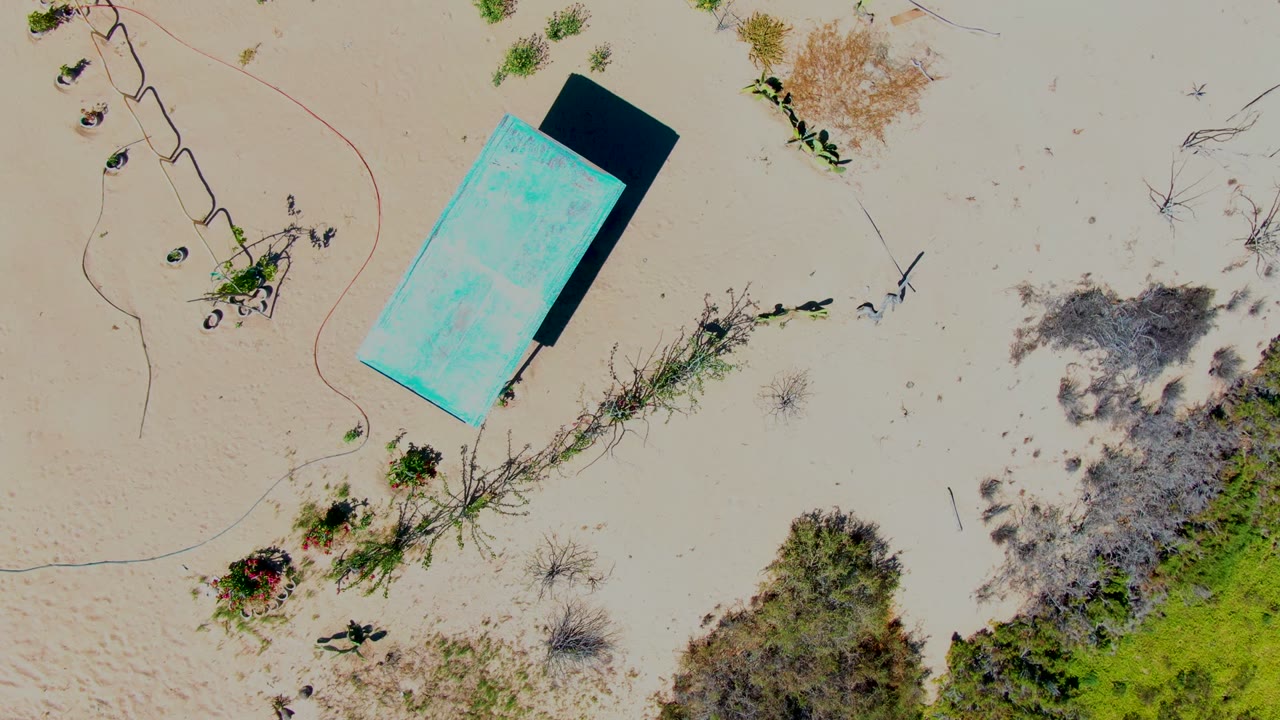 Aerial view of a blue rectangular structure casting a shadow on sand.