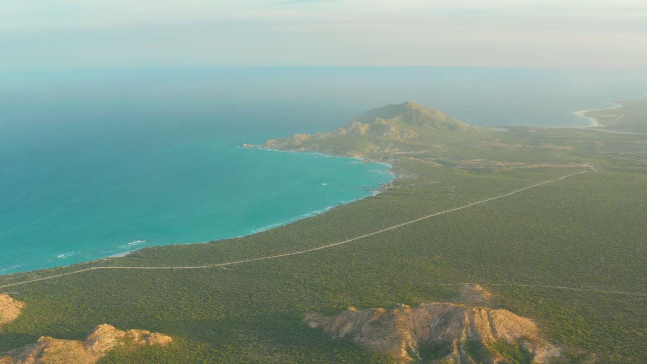 Coastal road crossing green scrubland beside a bright turquoise bay.