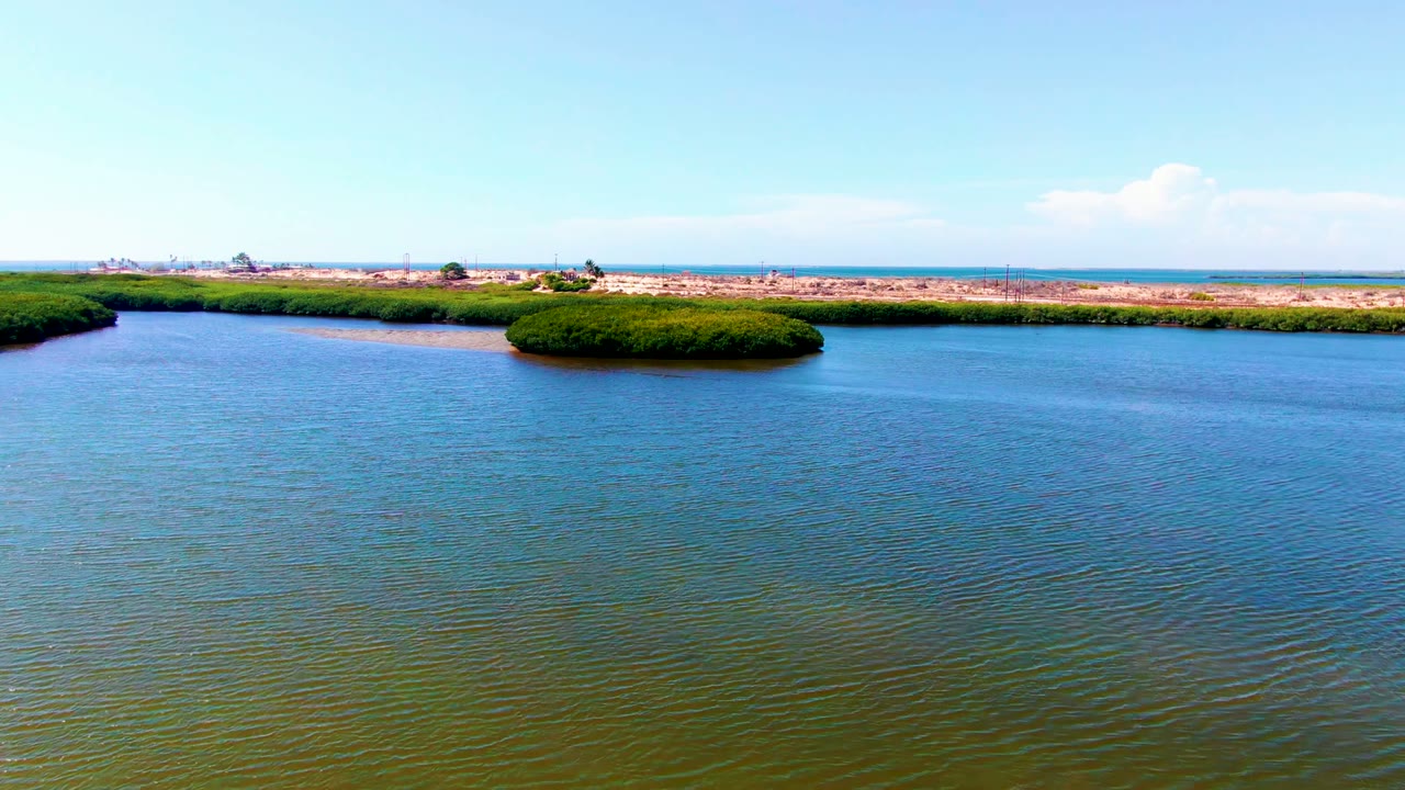 Opening frame of a San Carlos, Baja California Sur waterway with rippled blue-green water, a small green island near center, dry shore in the distance, and no visible people.