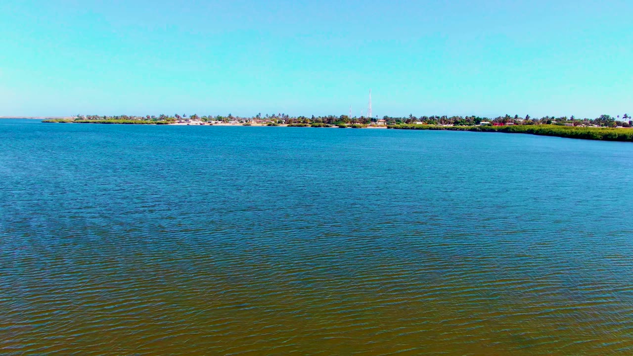 Rippling open water below a distant strip of trees and buildings.