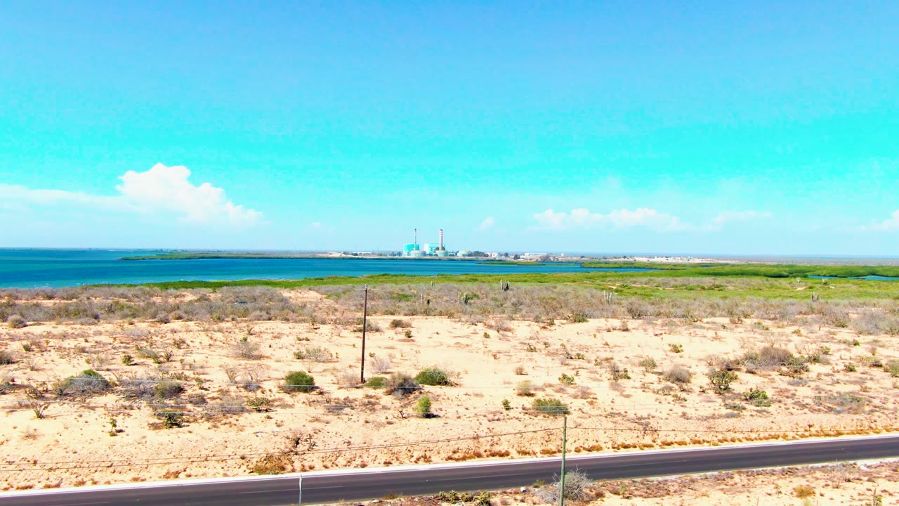 Sandy scrubland beside road with ocean and distant mosque-like structure