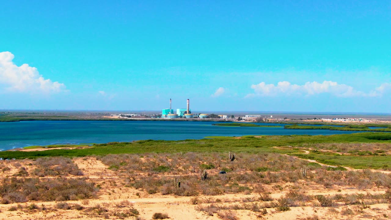 Arid scrub foreground with water channel and industrial towers in the distance