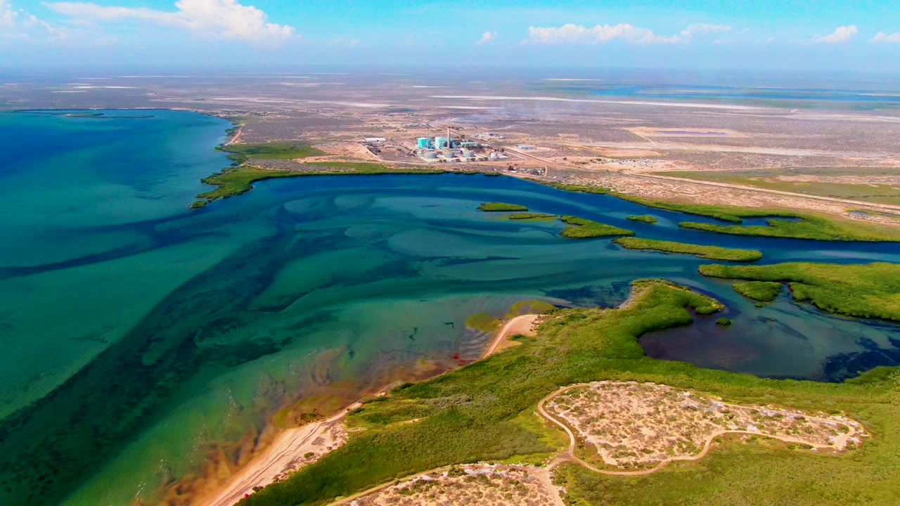 Wide aerial view of shallow blue-green waterways winding around marsh islands and sandy ground.