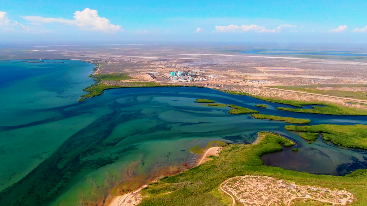 Two seconds into the San Carlos clip, the wide drone view shows green marsh islands separating shallow water, exposed sand, dry flats behind the coast, a low horizon, and no visible people.