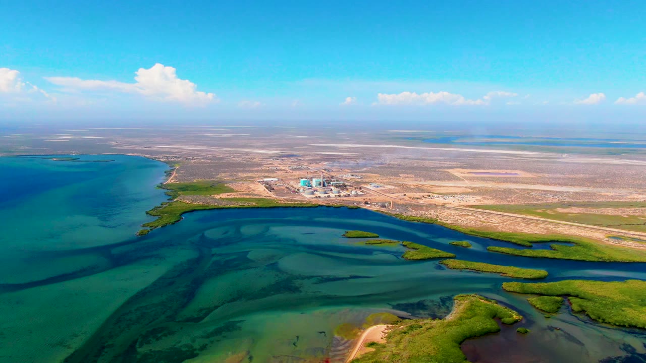 Opening frame over San Carlos, Baja California Sur showing shallow turquoise water, green marsh strips, sandy shoreline, distant flat land, and no visible people.