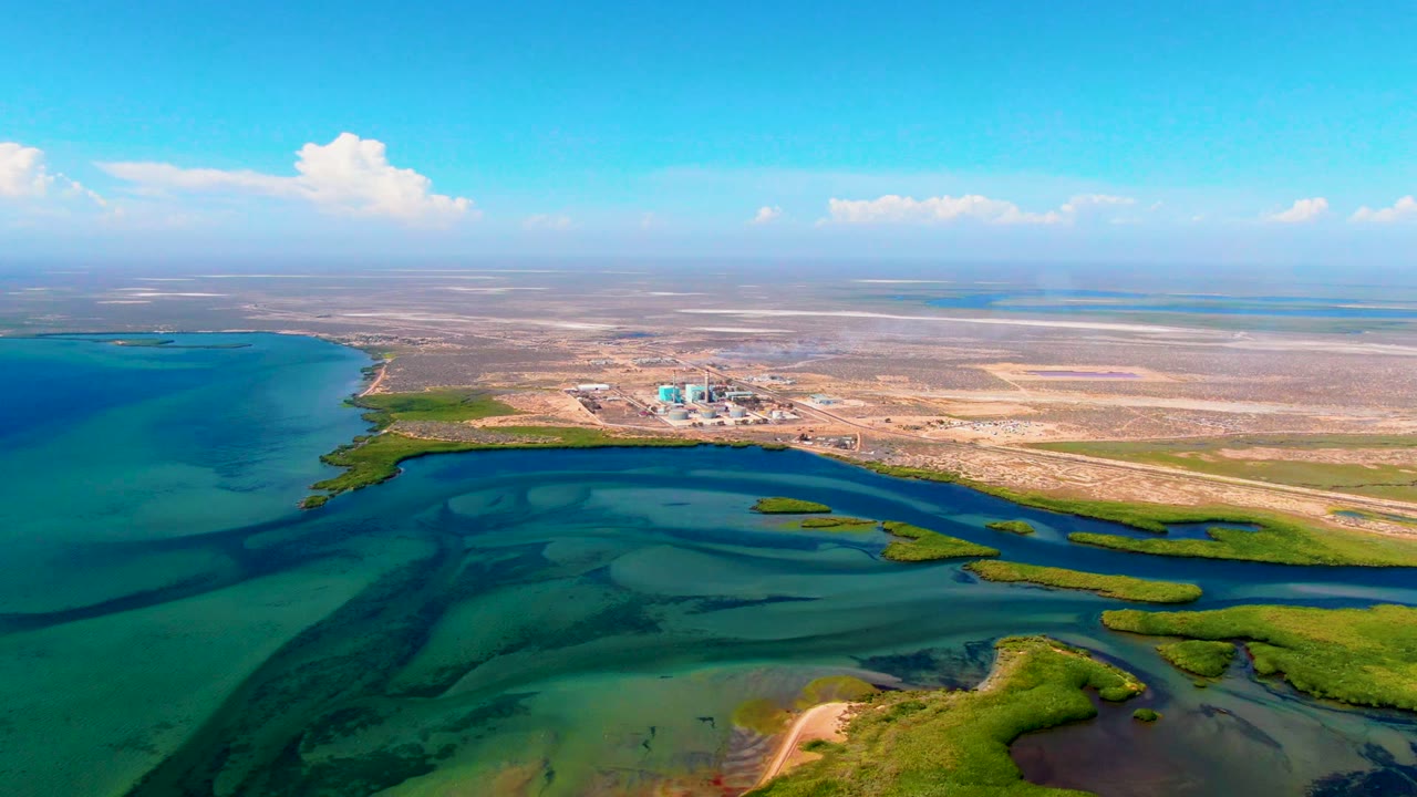 Wide drone view of turquoise water channels, green wetlands, and a dry coastal plain.