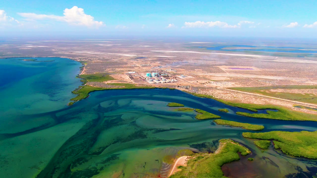 Wide drone view of marsh islands and blue water near dry terrain.