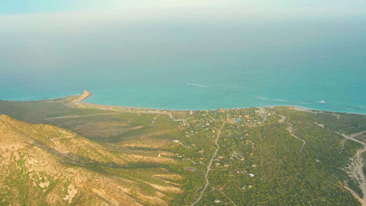 Wide aerial coastal view with hillside, roads, buildings, and ocean.