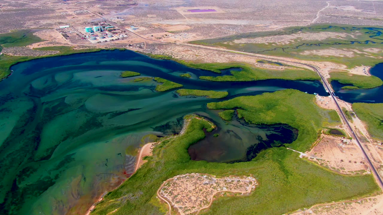 Drone view of a vehicle on a road beside turquoise water and green marsh areas.