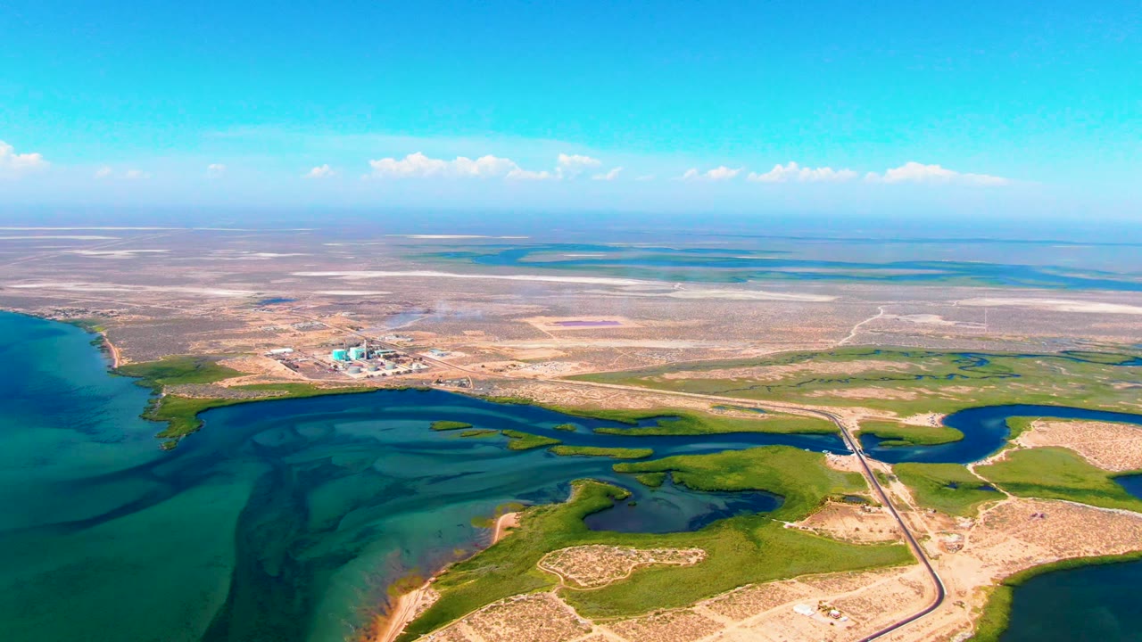 Coastal lagoon and wetlands with road access and an industrial plant inland.