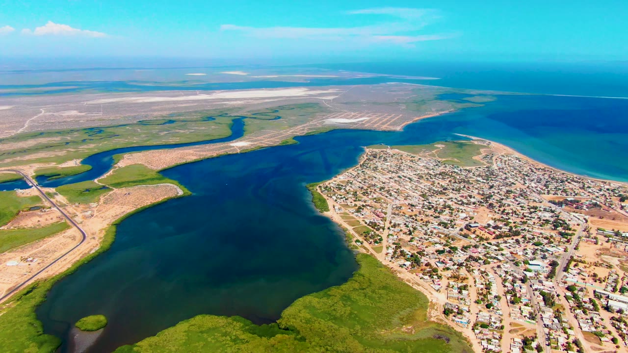 High aerial view of lagoon water, wetlands, sandy coast, and town blocks.