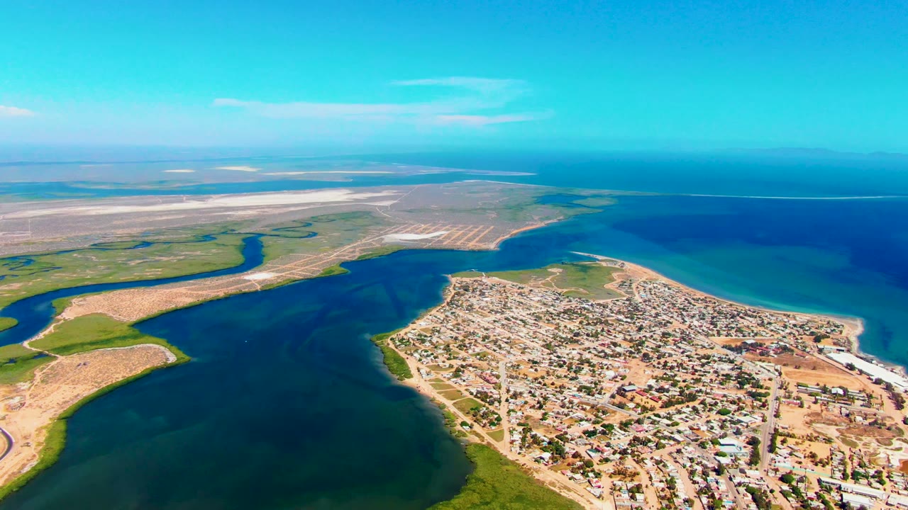 Drone view over a coastal settlement, inlet water, and sandy flats.