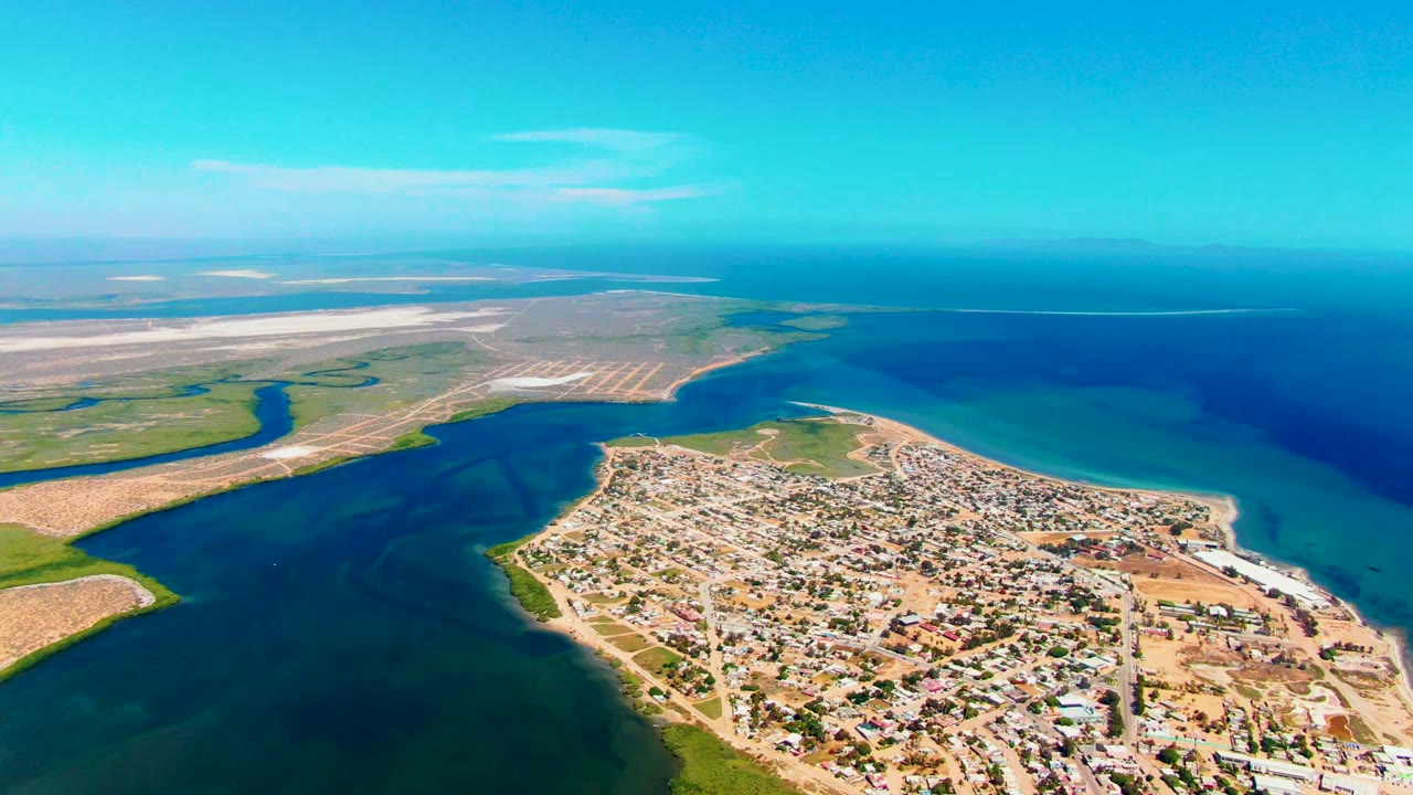 Drone view of town, shoreline, ocean, and pale sandy land.