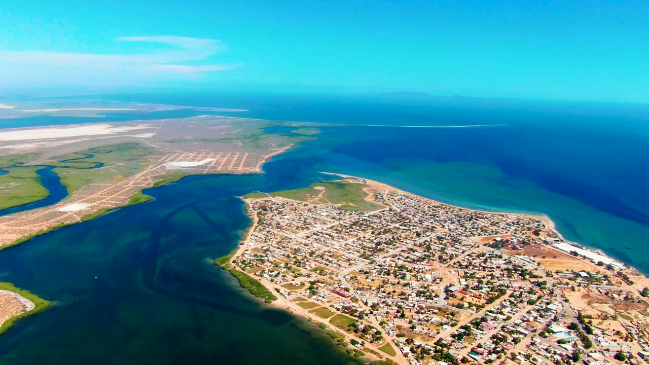 Wide drone view of town, inlet, shoreline flats, and blue-green water.