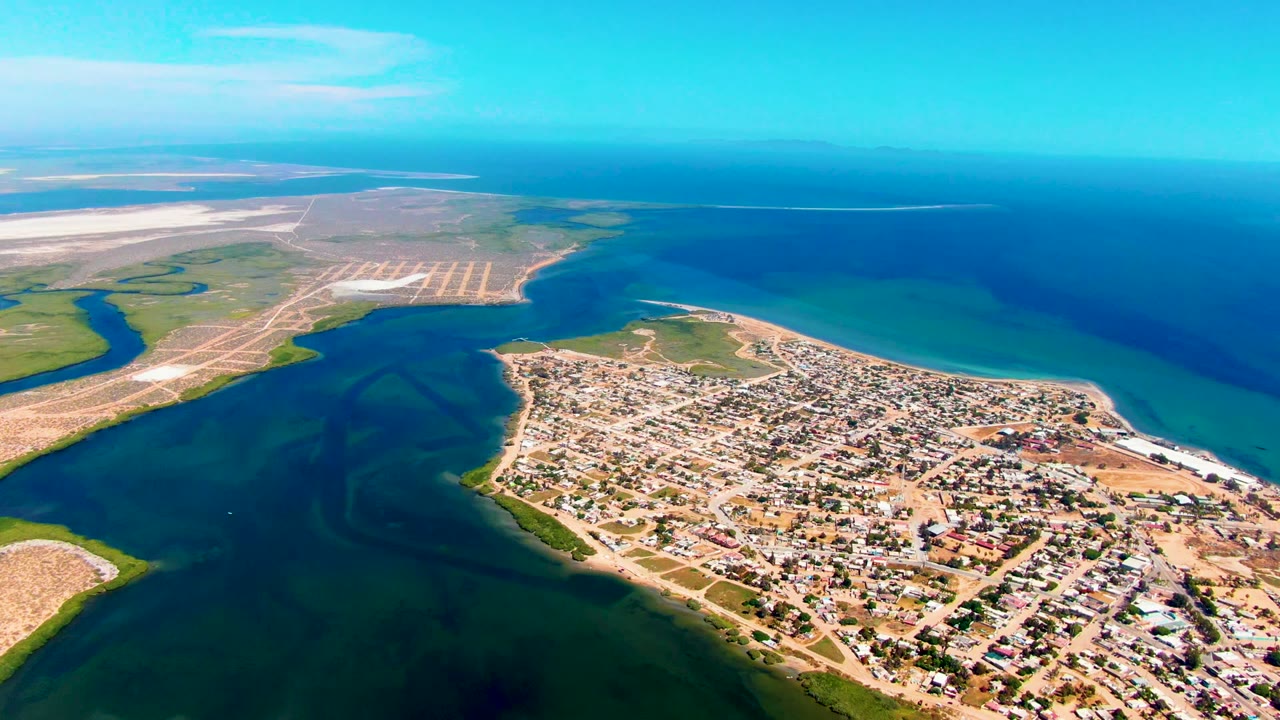 Drone view of a sandy coastal town between tidal water and open ocean.