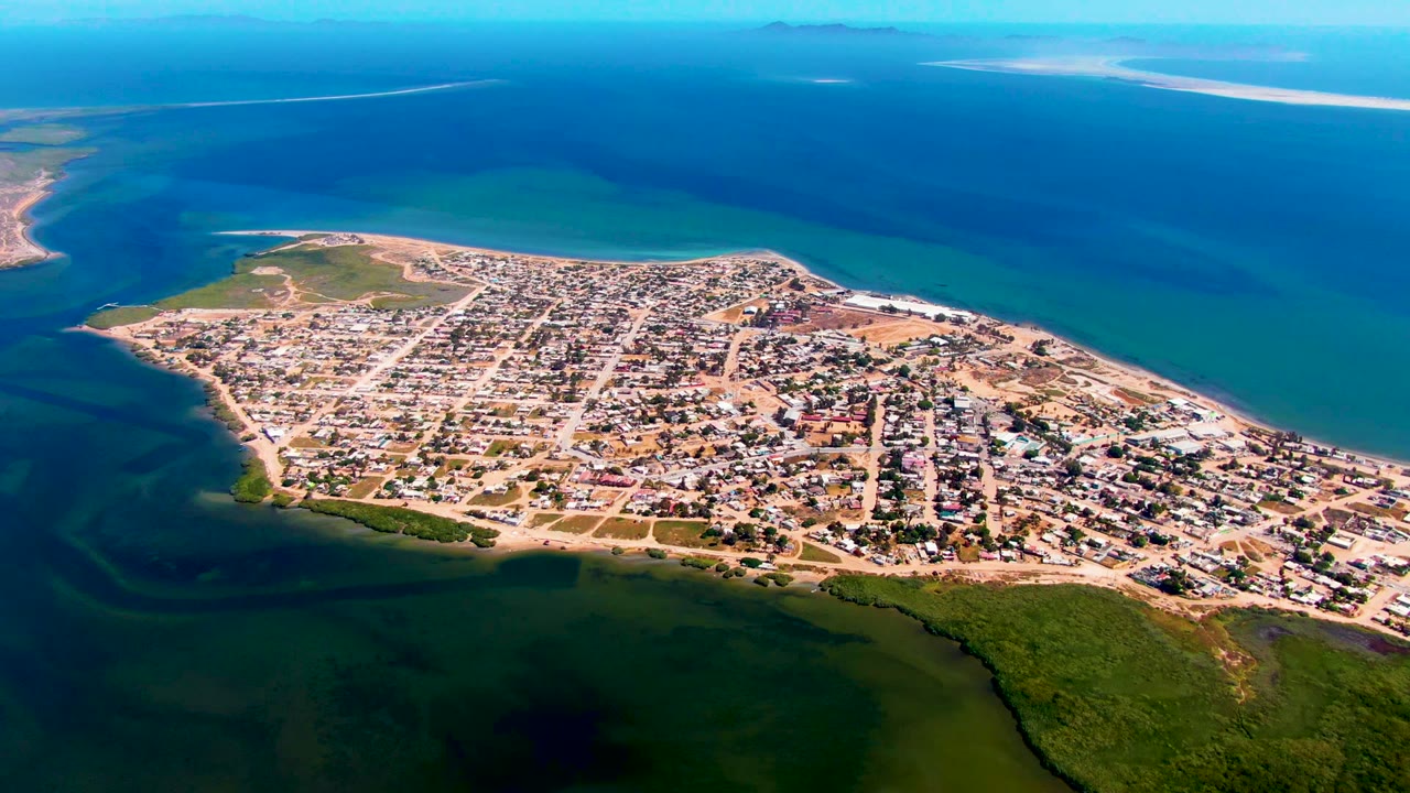 Coastal town grid with roads and low buildings beside turquoise water.