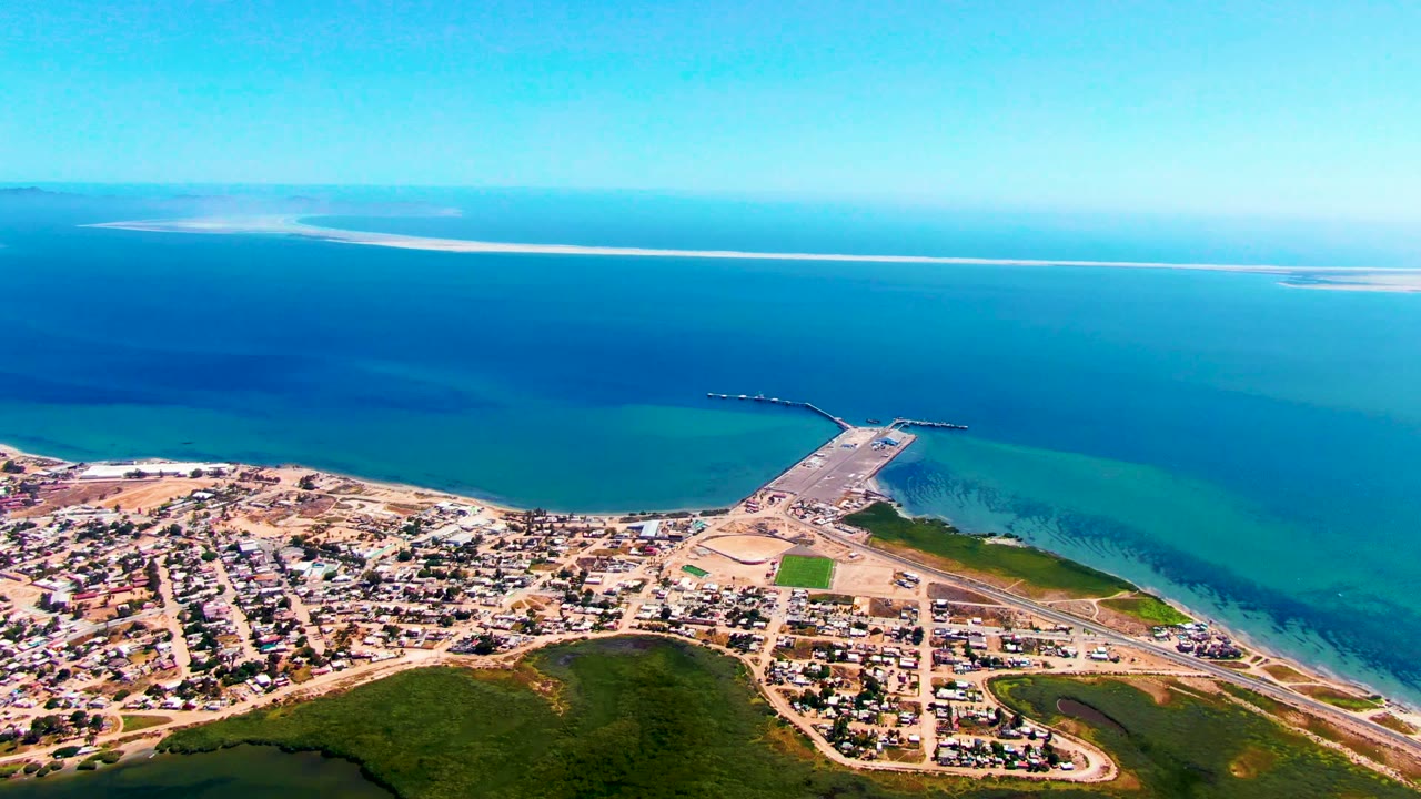Drone view of houses, shoreline, pier, and open sea.