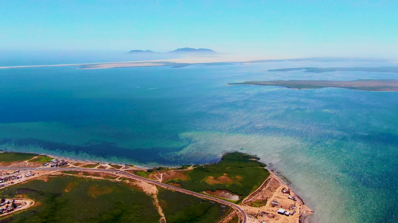 Drone view over shallow blue water and a shoreline road.