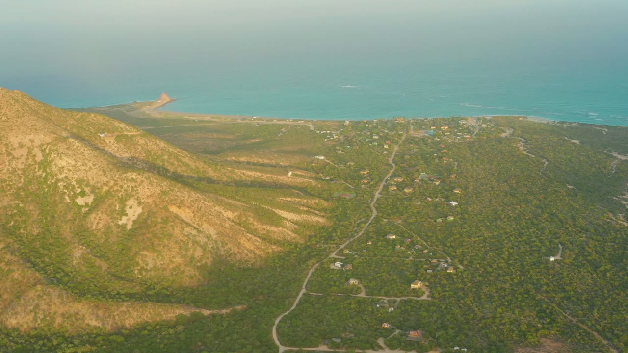 Wide aerial coastal valley with hillside, roads, beach, and ocean horizon