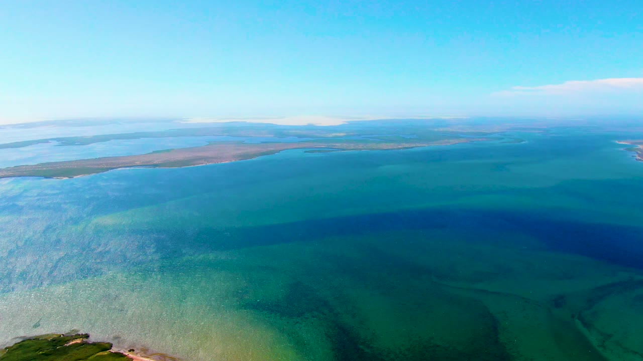At 0:02, San Carlos coastal water fills most of the frame with visible depth color changes, low brown-green land across the horizon, a small cloud, and no visible people.