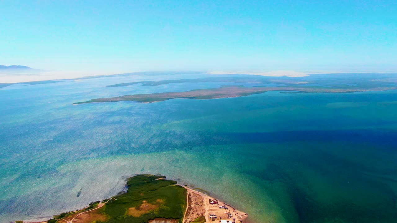 Third frame holds the San Carlos coastal composition, with green vegetation and sandy shoreline at the bottom, broad blue water beyond, and no visible people.