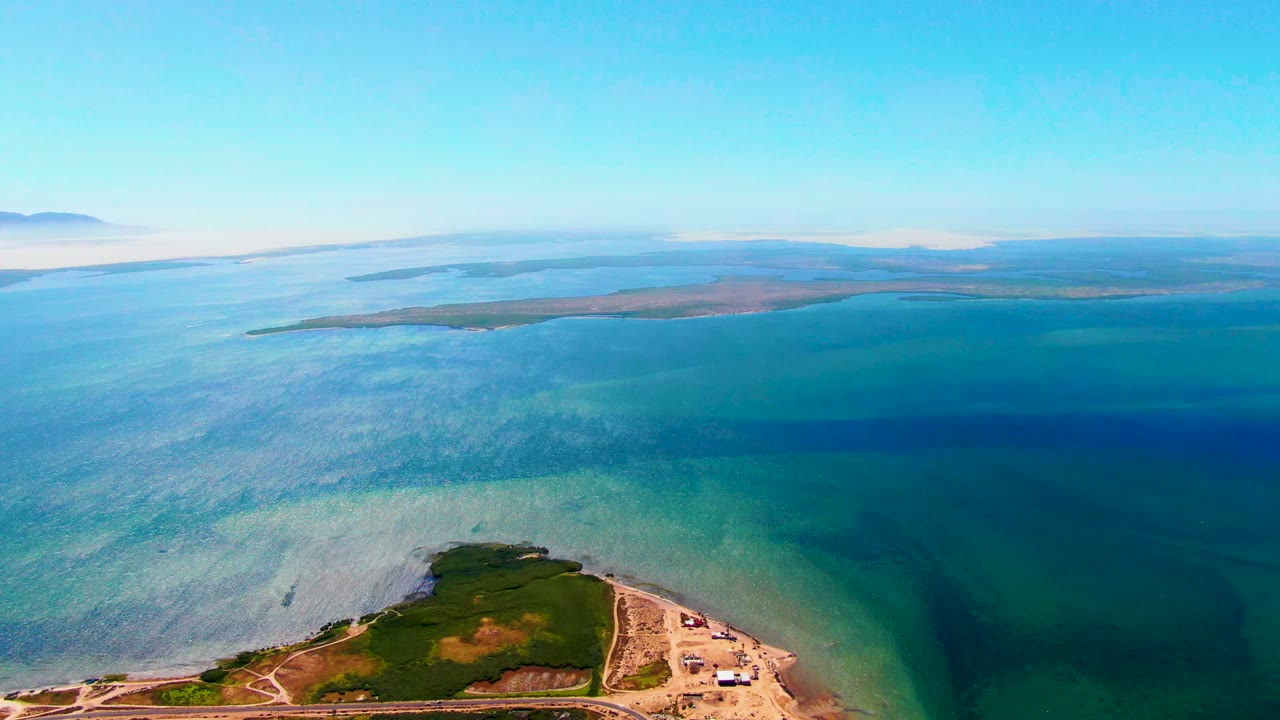 Drone view over blue coastal water with shoreline and distant land.