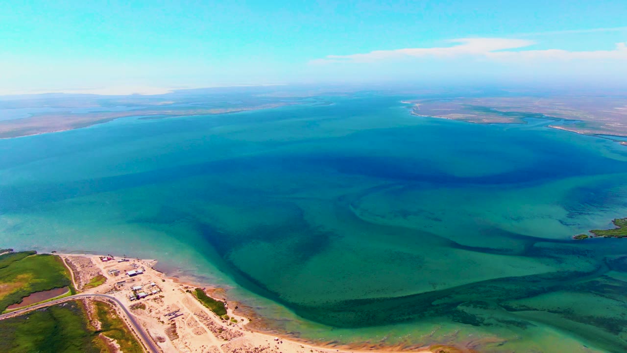 Drone view across blue-green water with beach structures at the lower edge.