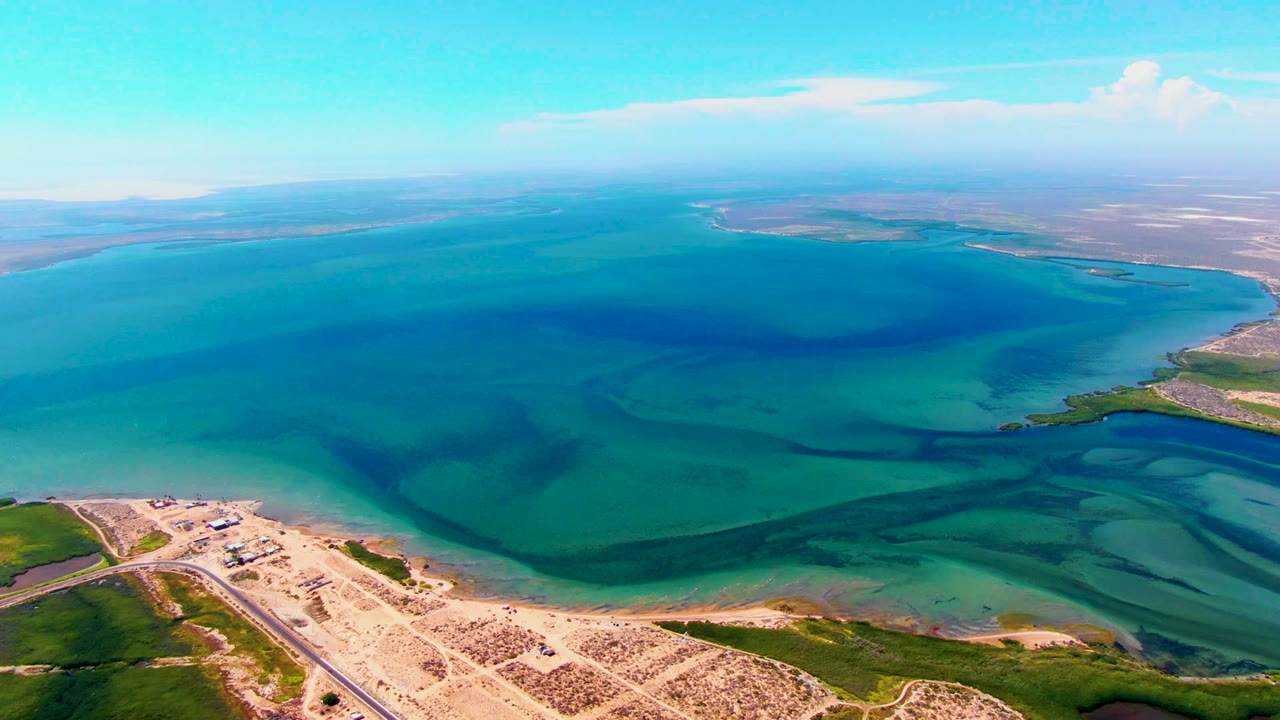 Aerial coastal water with dark shallow patterns and sandy shore below.