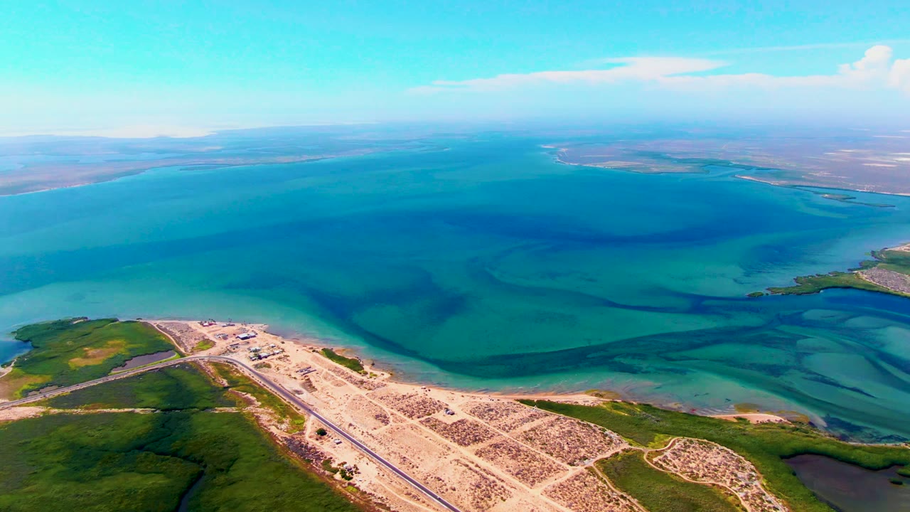 Drone view of coastal roads and turquoise water with distant shoreline