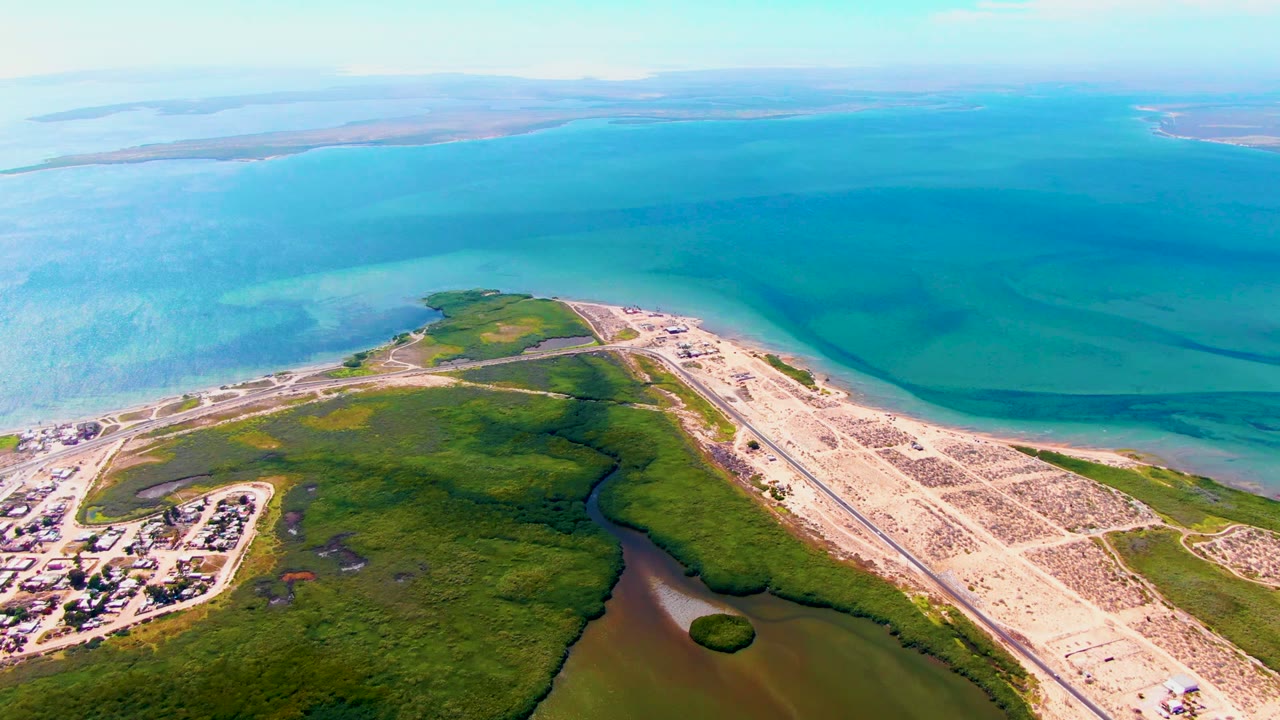 Drone view of runway land, marsh channels, buildings, and blue coastal water.