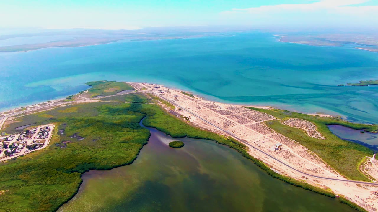 High aerial view of vehicles on a pale causeway beside marsh and ocean.
