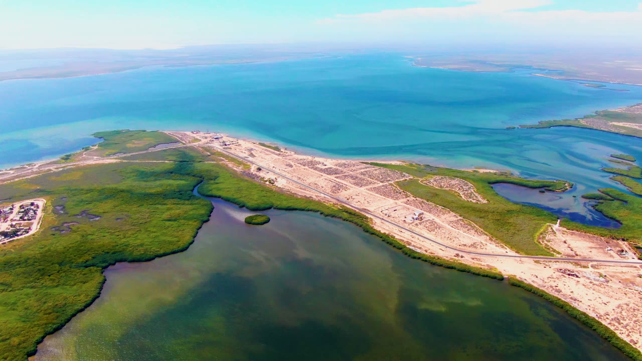 Aerial frame over San Carlos, Baja California Sur showing turquoise water beyond sandy coastal roads and green wetland vegetation, with no visible people.