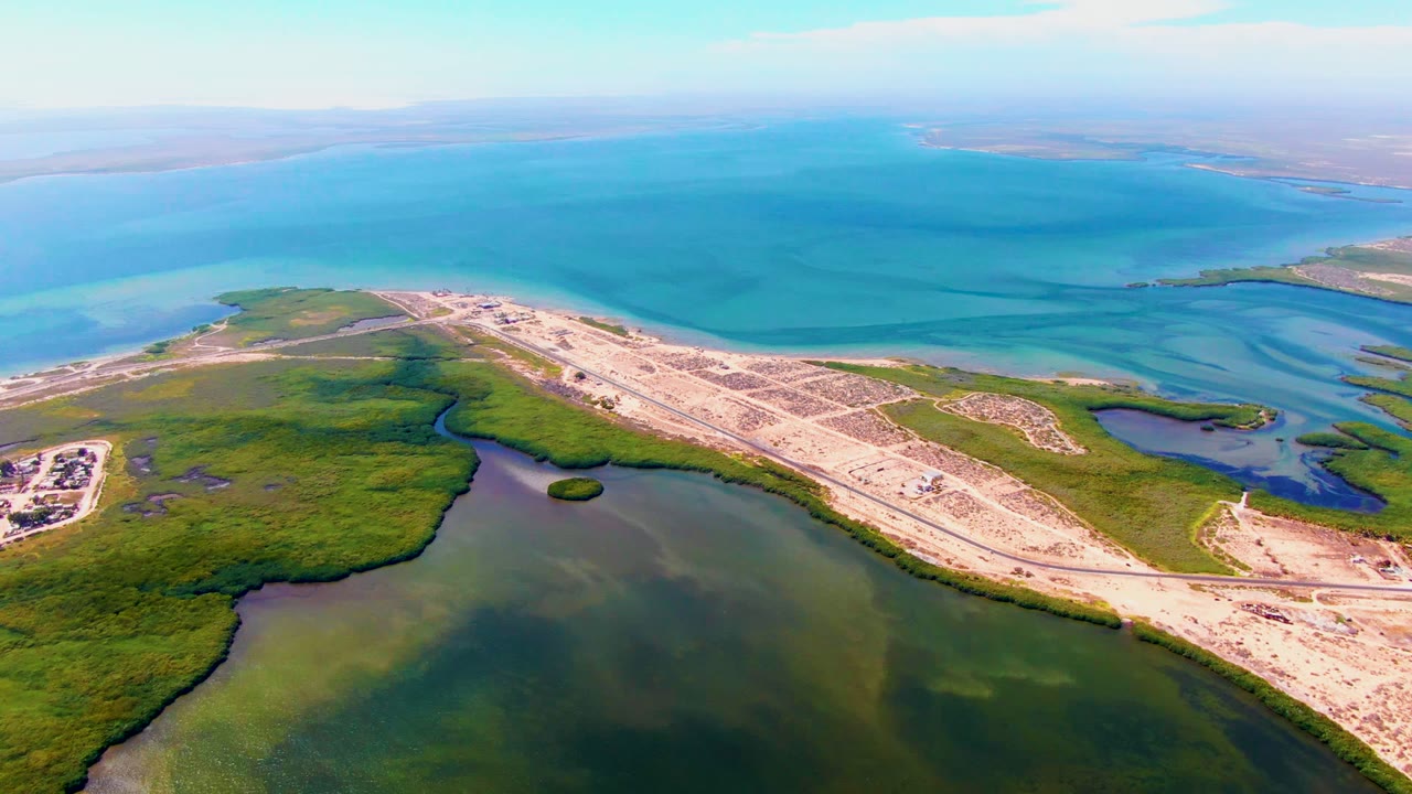 Drone view across marsh vegetation, shallow water, sandy lots, and blue sea.