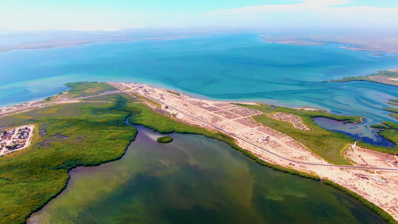 High aerial frame over San Carlos, Baja California Sur showing a pale sandy grid beside green wetlands and expansive blue coastal water, with no visible people.