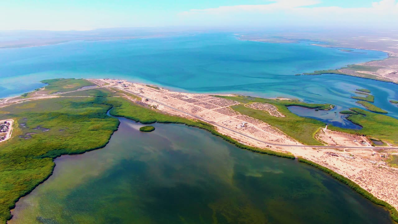 High aerial view of sandy road development between wetland water and ocean.