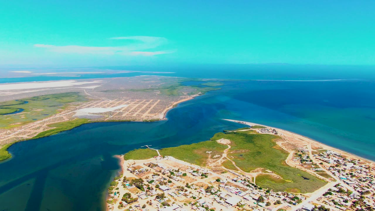 Aerial coastal inlet with turquoise water beside sand flats and low green land.