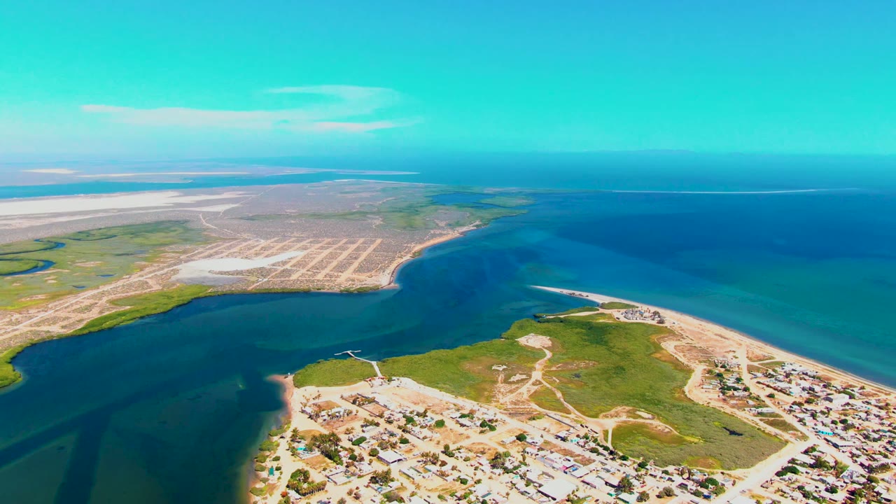 High aerial frame over San Carlos, Baja California Sur showing the inlet mouth, gridded pale sand area, green marsh-like shoreline, open blue water, and no visible people.