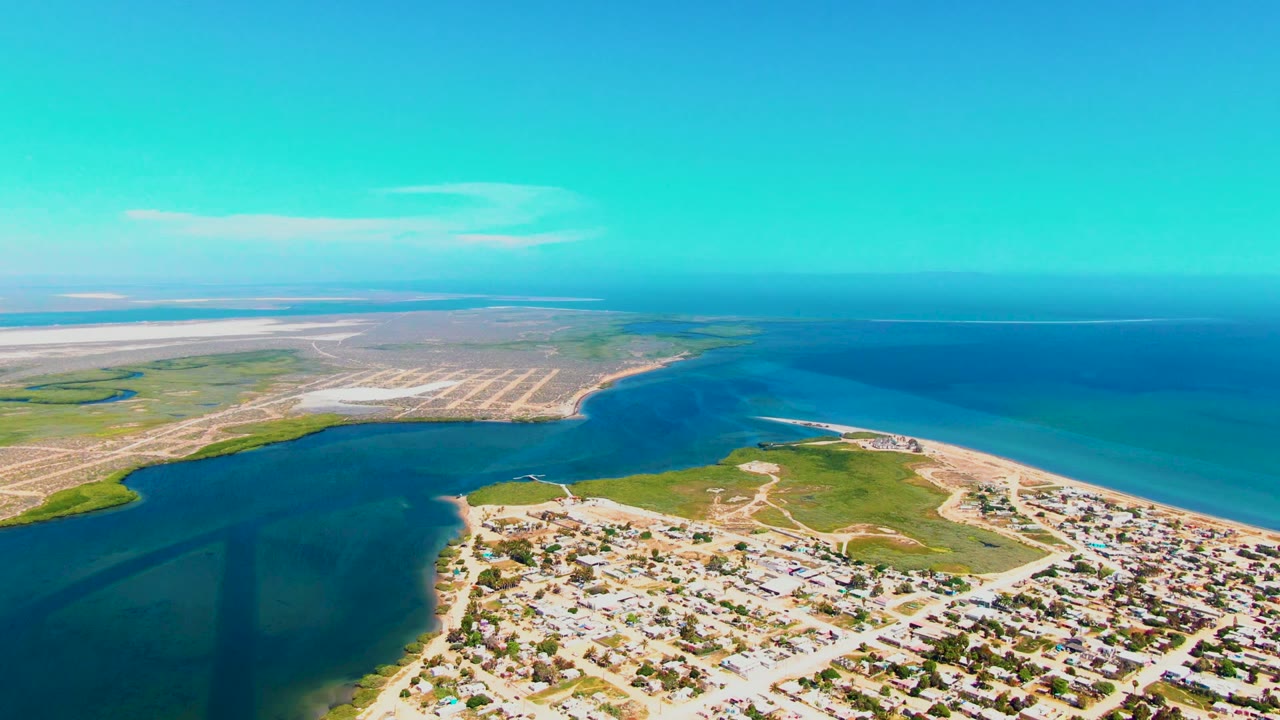 Aerial coastline with inlet water, sandy flats, houses, and clear blue sky.