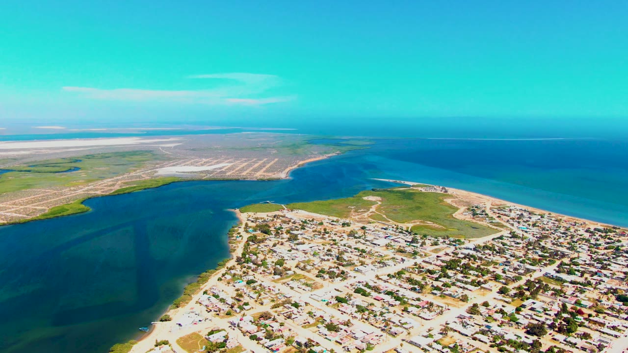 Opening aerial frame over San Carlos, Baja California Sur, with deep blue coastal water beside patterned fields and a residential shoreline, no visible people.