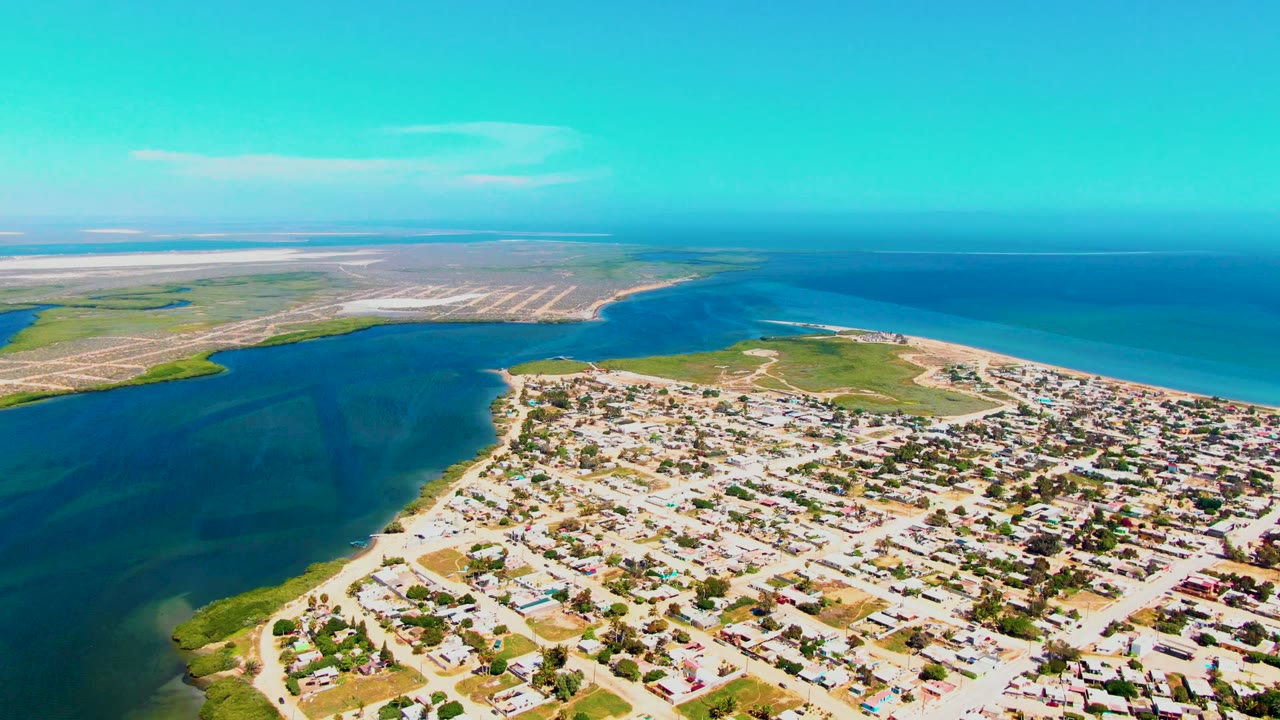 Wide drone view of houses, shoreline, inlet, and open water.