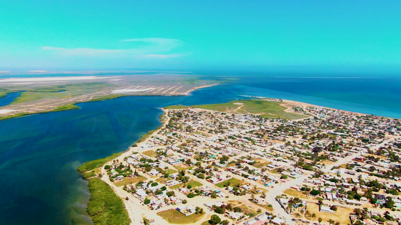 Drone view of residential blocks, shoreline vegetation, inlet water, and open ocean.