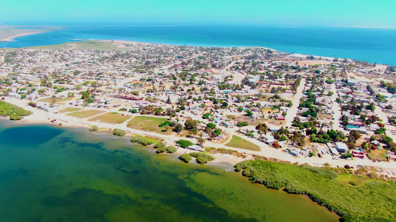 Wide aerial over coastal homes beside green lagoon water and blue ocean.