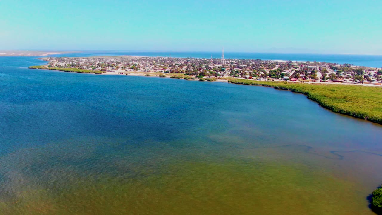 Drone view of calm water leading to a shoreline town under a clear sky.