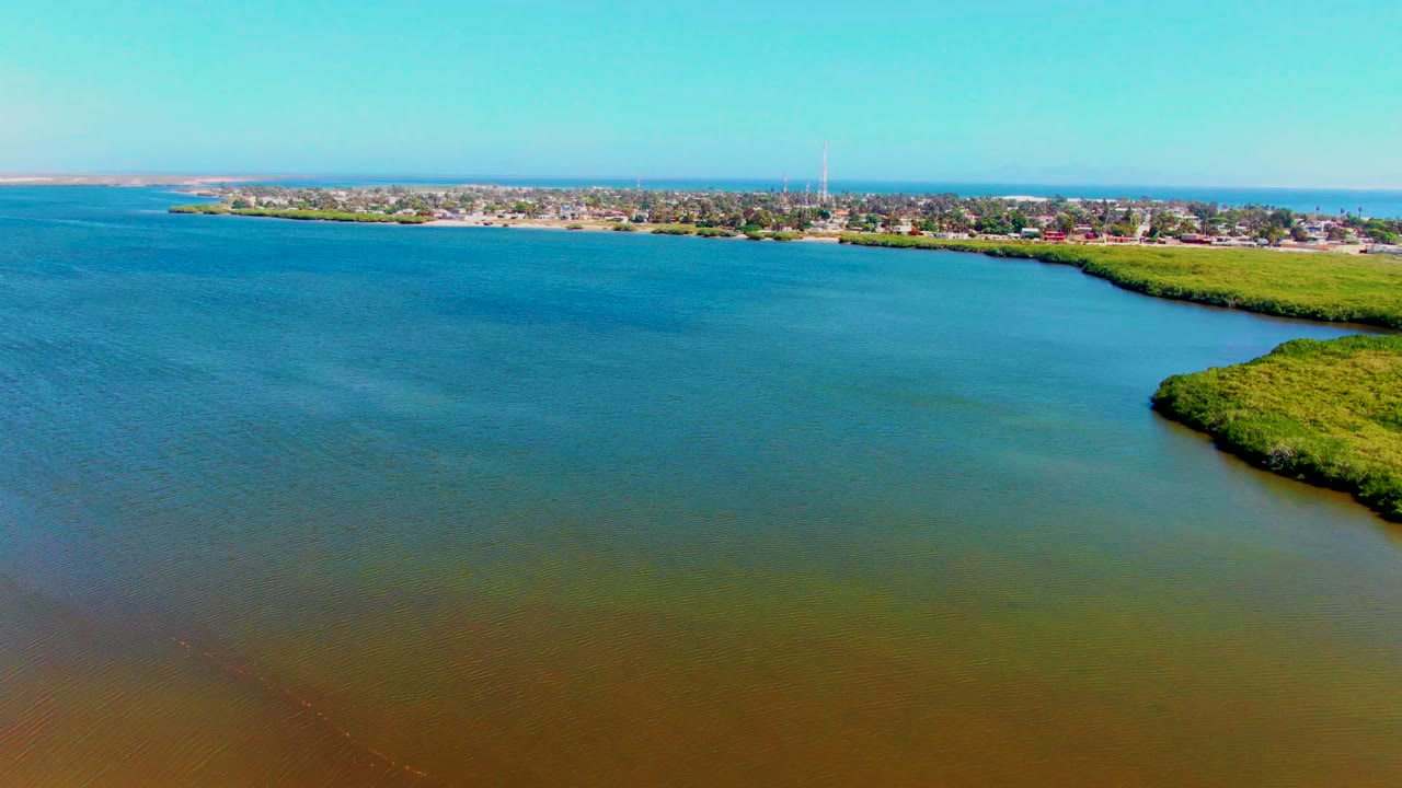 Wide aerial of blue and brown estuary water with town beyond the shoreline.