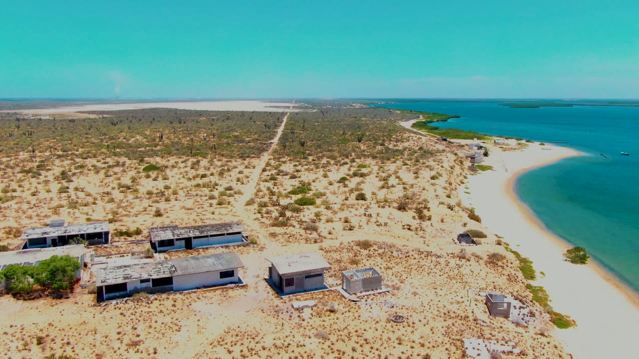 Drone view of sandy coastal ruins with scrubland, beach, and turquoise water.