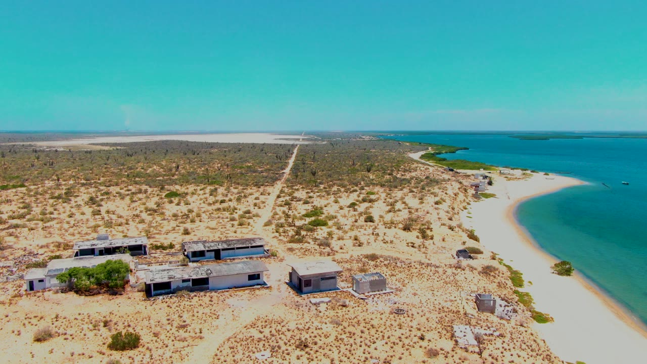 Elevated shoreline view with arid land, beach buildings, and blue coastal water.
