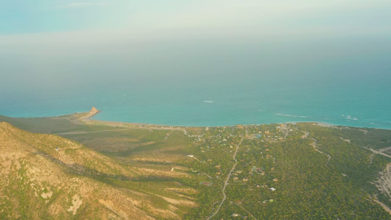Wide aerial coast view with hillside foreground and small shore structure.