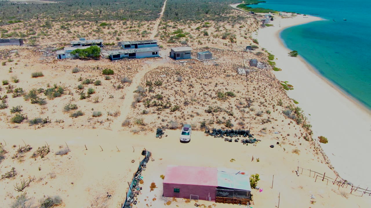 Drone view of desert lots, low buildings, road, beach, and blue water.